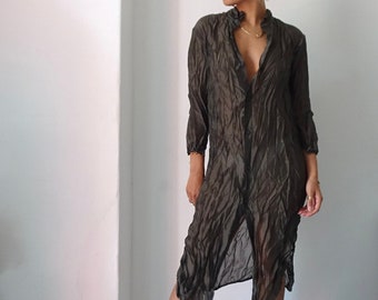 Könnte beinhalten: Eine Frau trägt ein langes, olivgrünes, durchsichtiges Hemdblusenkleid mit Rüschenkragen. Sie trägt schwarze Plateausandalen und goldene Creolen.