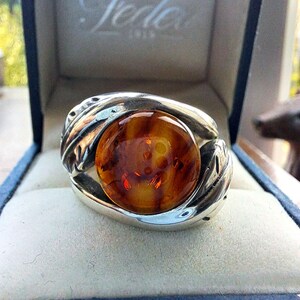 May include: A silver ring with a large amber stone set in the center. The ring has a detailed design with intricate carvings.