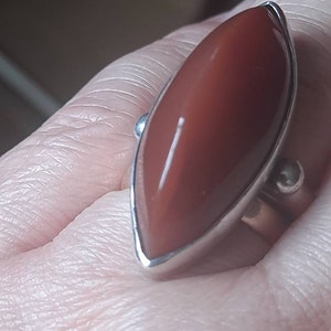 May include: A silver ring with a large, reddish-brown, marquise-shaped gemstone.