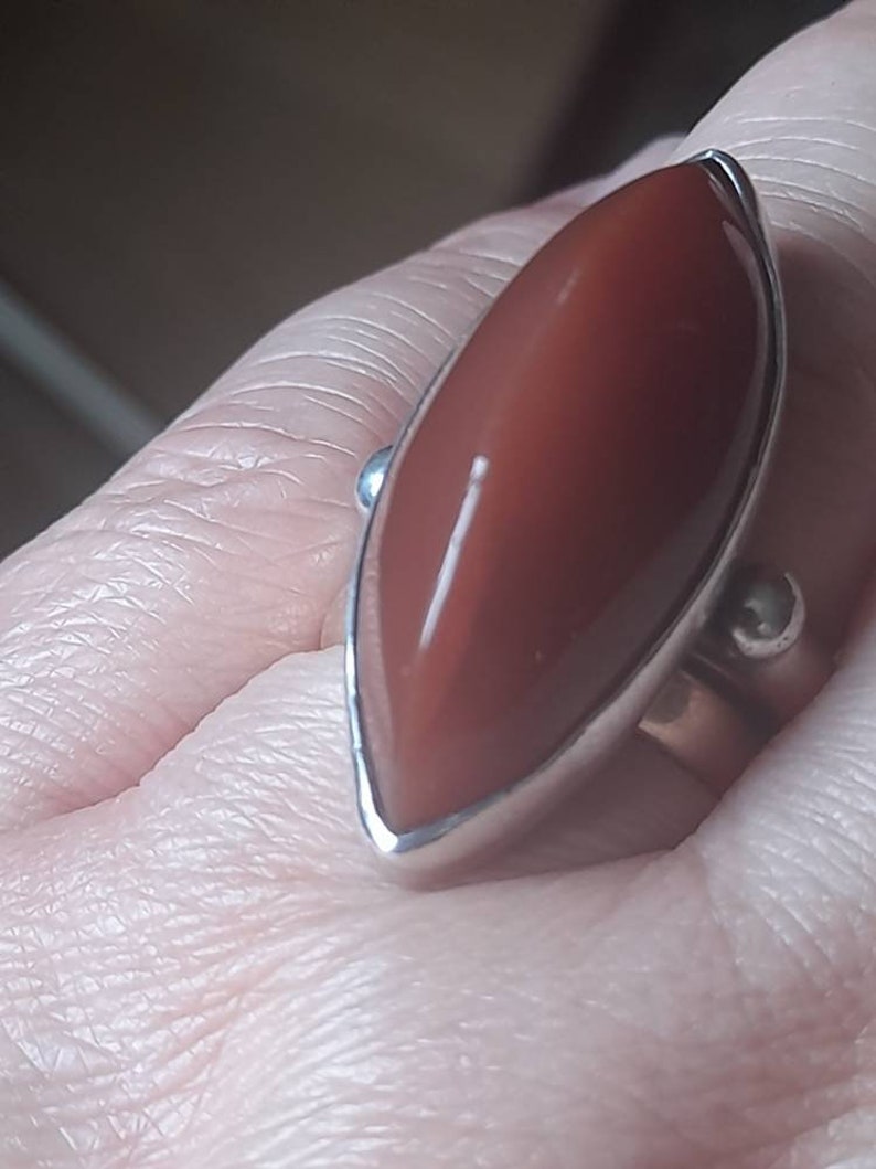 May include: A silver ring with a large, reddish-brown, marquise-shaped gemstone.