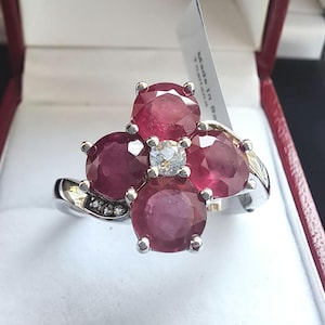 Può includere: Anello in argento con un design floreale, con quattro grandi pietre preziose rotonde rosso intenso e una piccola pietra preziosa trasparente al centro. Piccole pietre trasparenti accentuano la fascia. Presentato in un cofanetto rosso.