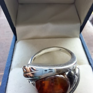 May include: A silver ring with a large amber stone set in a snake design. The ring is in a blue velvet box.