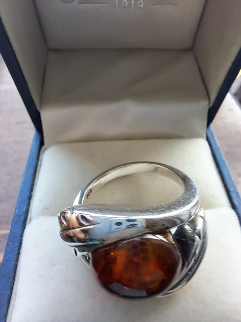 May include: A silver ring with a large amber stone set in a snake design. The ring is in a blue velvet box.