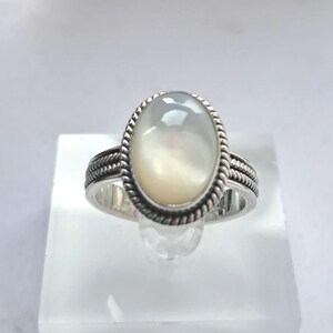 May include: A silver ring with a white oval mother of pearl gemstone. The ring has a rope-like design around the band and the gemstone.