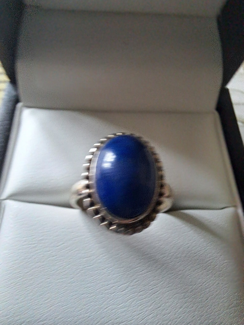 May include: A silver ring with a large, oval-shaped blue gemstone set in a decorative silver bezel.