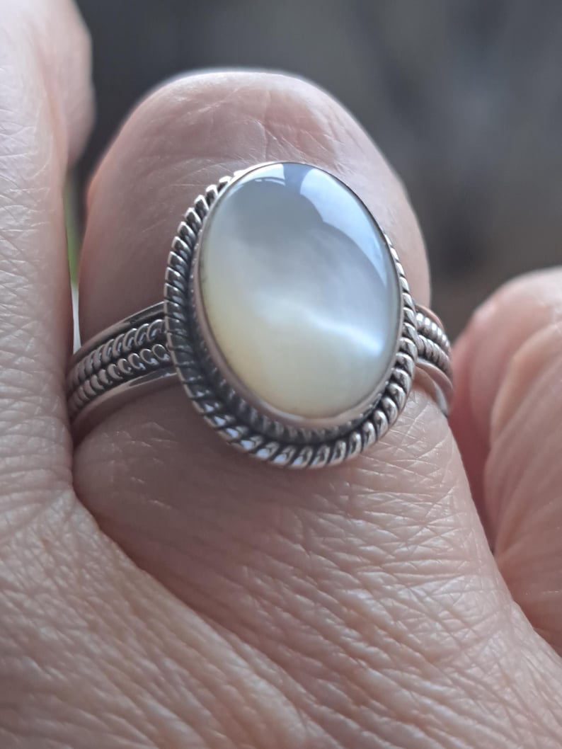 May include: A silver ring with a white oval gemstone set in a rope-like design.