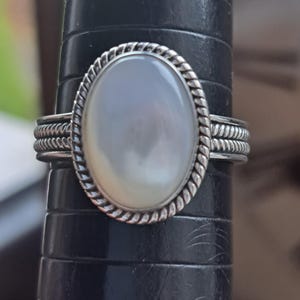 May include: A silver ring with a white oval-shaped gemstone set in a rope-like design.