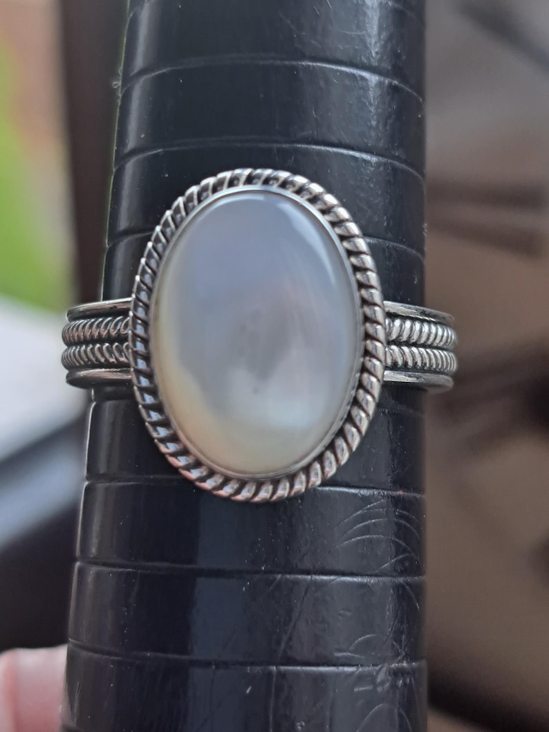 May include: A silver ring with a white oval-shaped gemstone set in a rope-like design.
