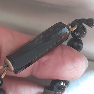 May include: A black beaded necklace with a long, faceted black glass bead with a gold metal clasp.