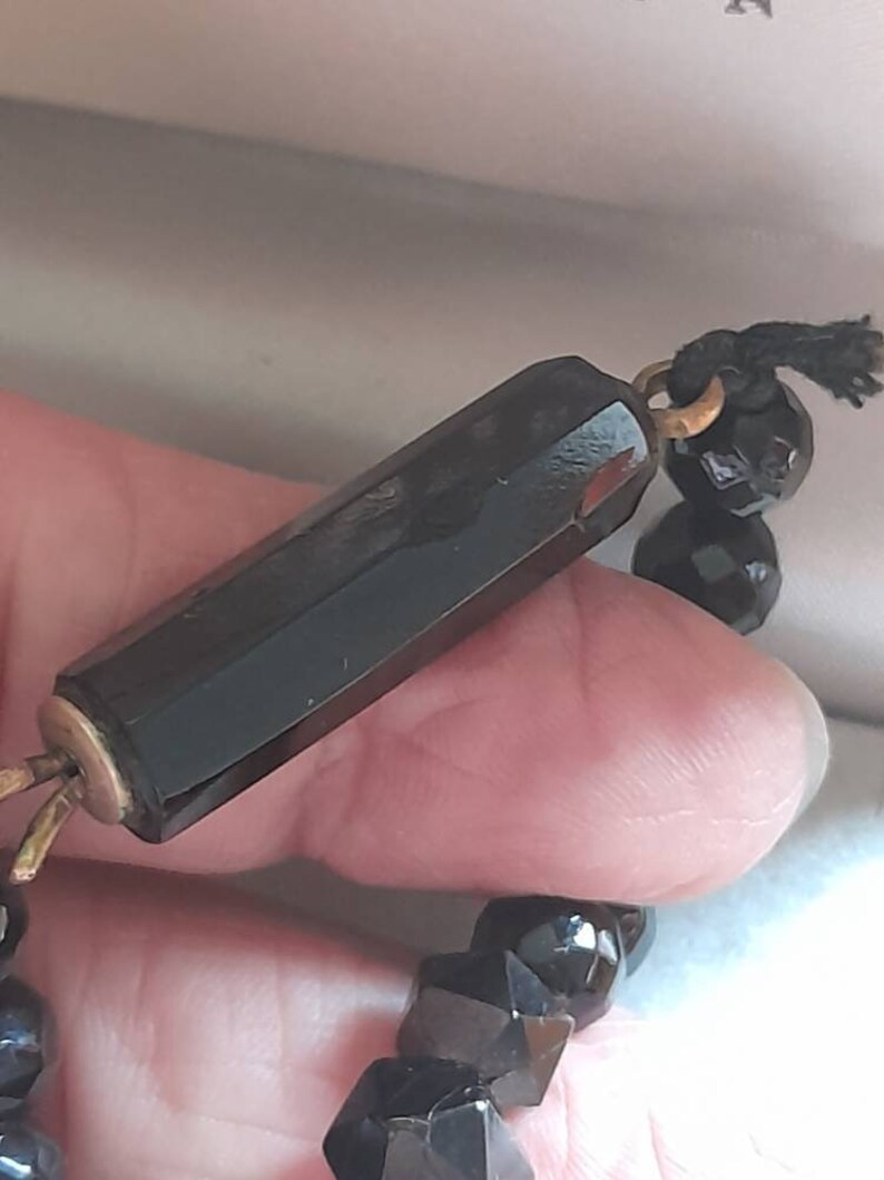 May include: A black beaded necklace with a long, faceted black glass bead with a gold metal clasp.