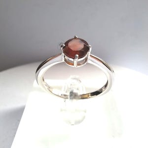 Op de afbeelding: Een zilveren ring met een ronde, donkerrode edelsteen.