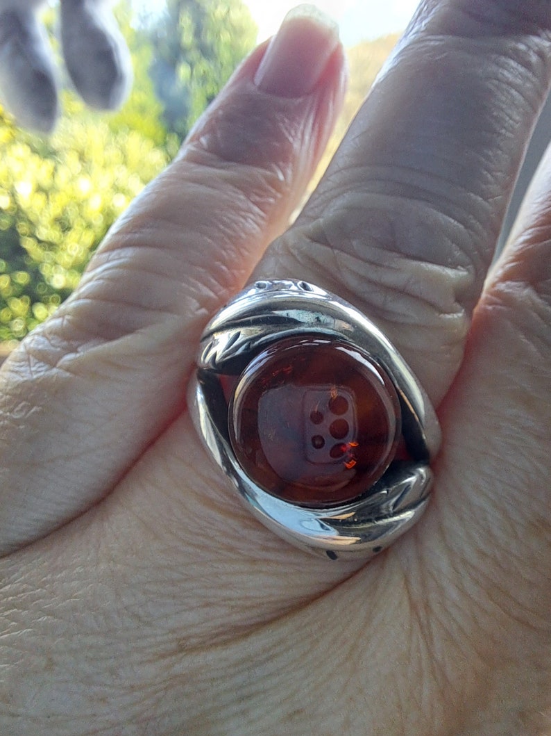 May include: A silver ring with a large, round, amber stone set in the center. The ring has a detailed design around the stone.
