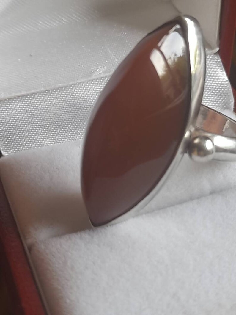 May include: A silver ring with a large, oval-shaped, reddish-brown gemstone.