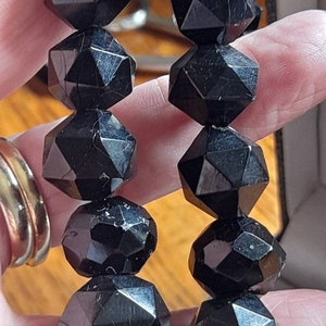 May include: A black gemstone necklace with faceted beads. The beads are shaped like a star with many points. The necklace is made of natural black obsidian.