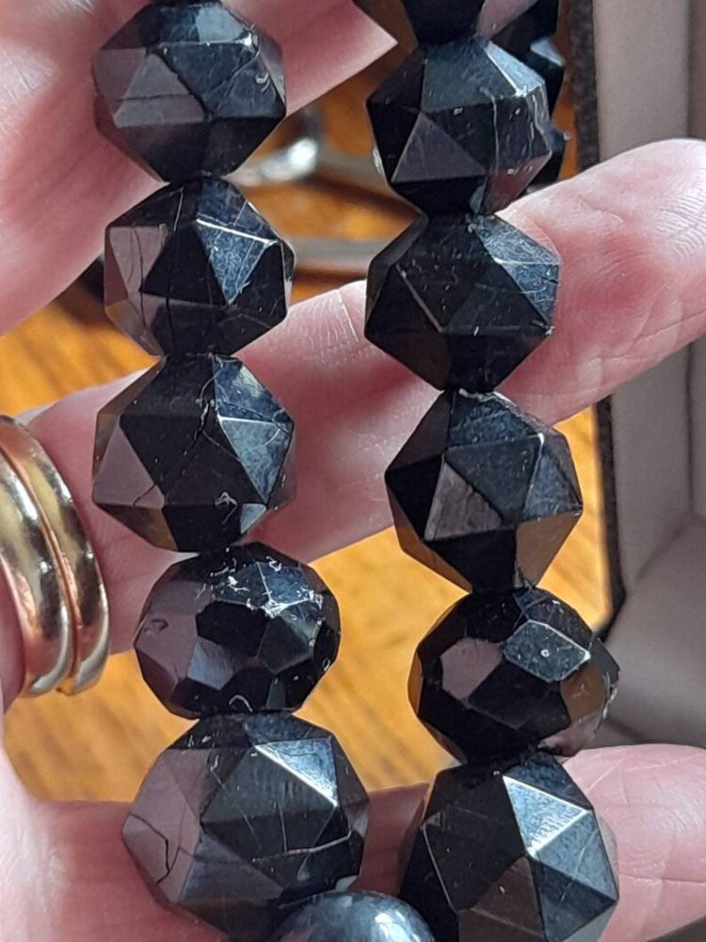 May include: A black gemstone necklace with faceted beads. The beads are shaped like a star with many points. The necklace is made of natural black obsidian.