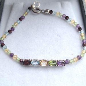 May include: A silver bracelet featuring a range of gemstones, including amethyst, garnet, aquamarine, citrine, peridot, and topaz.