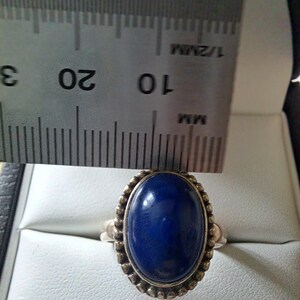 May include: A silver ring with a dark blue oval gemstone set in a beaded bezel. The ring is measured against a ruler.