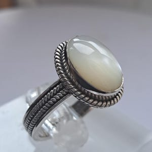 May include: A silver ring with a white oval-shaped gemstone set in a rope-like design.