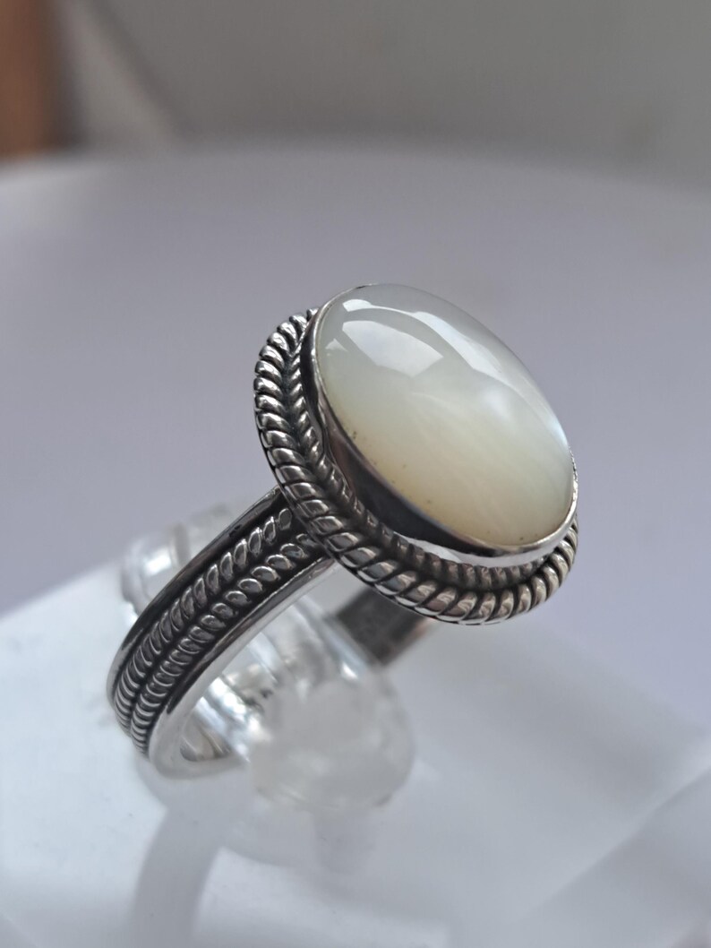 May include: A silver ring with a white oval-shaped gemstone set in a rope-like design.