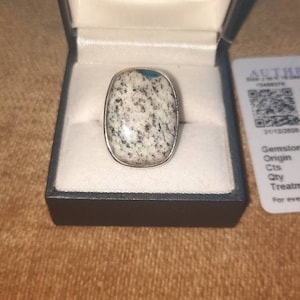May include: A silver ring featuring a large oval-shaped blue and white gemstone. The ring is displayed in a white box with the inscription "Charles Edwards" inside.