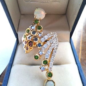 May include: A gold ring with a unique design featuring a cluster of colorful gemstones, including green, blue, red, and white. The ring is set with a large white opal on each end.