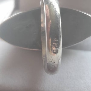 May include: A silver ring with a dark gray oval stone. The ring is marked with the number "925" on the inside band.