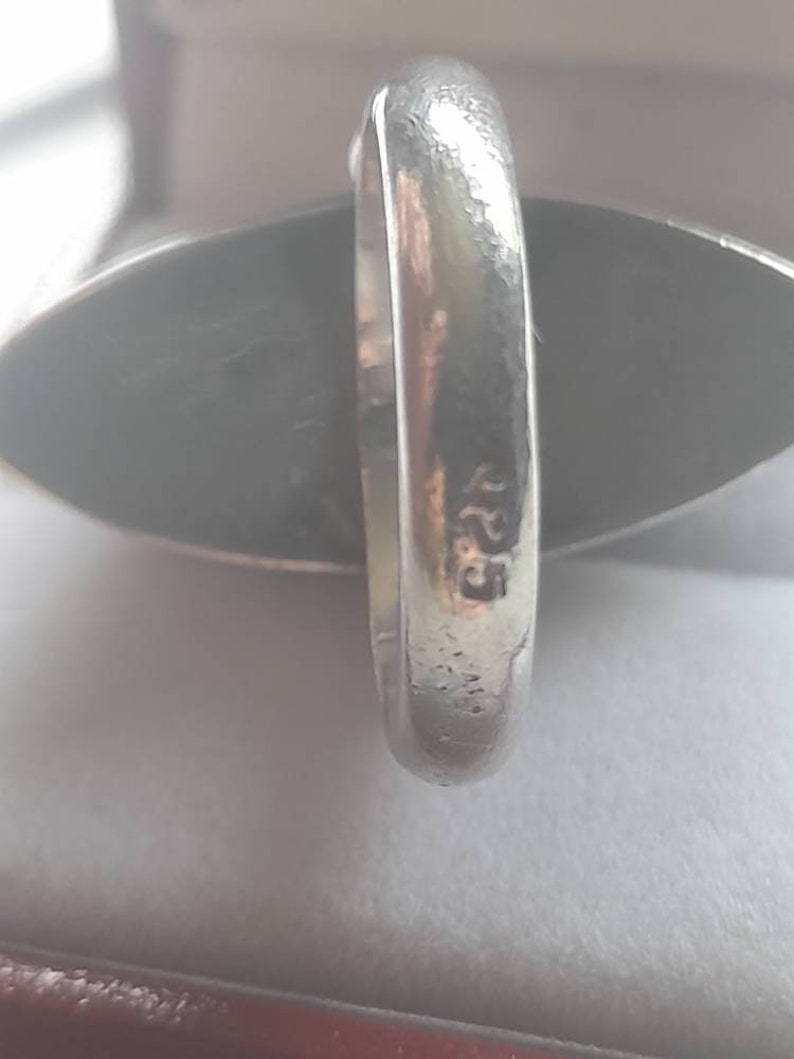 May include: A silver ring with a dark gray oval stone. The ring is marked with the number "925" on the inside band.