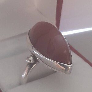 May include: A silver ring with a teardrop-shaped, reddish-brown gemstone. The ring is set in a silver band with a small, clear stone on the side.