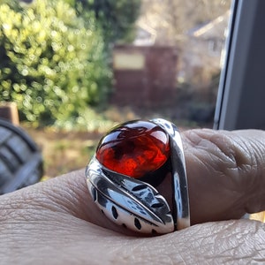 May include: A silver ring with a red gemstone set in a leaf design.