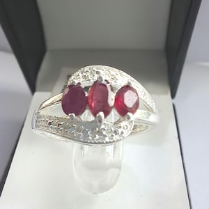 May include: A silver ring featuring three red gemstones and a row of smaller white gemstones.