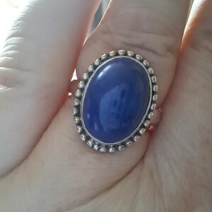 May include: A silver ring with a large oval blue gemstone set in a beaded bezel.