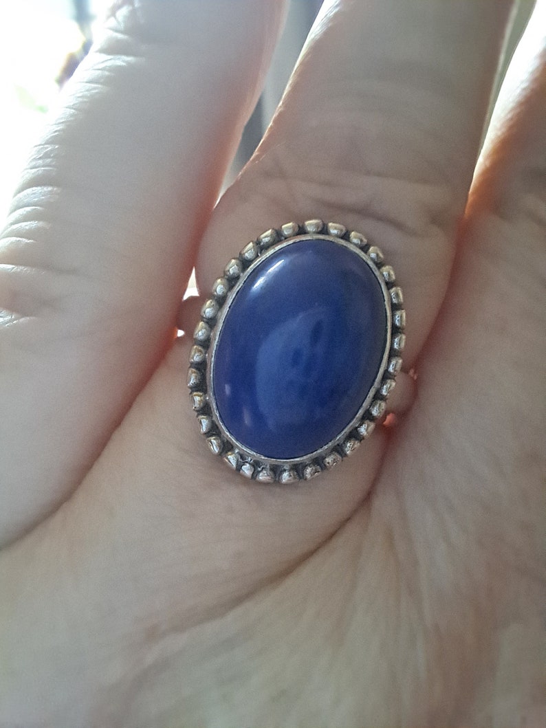 May include: A silver ring with a large oval blue gemstone set in a beaded bezel.