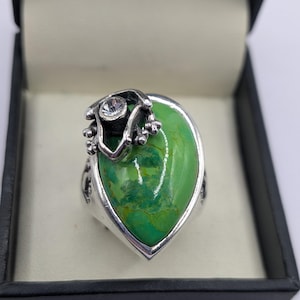 Peut inclure: Bague en argent avec une grosse pierre verte en forme de goutte d'eau. La bague a un accent décoratif en argent avec une petite pierre transparente. La bague est présentée dans un écrin noir.