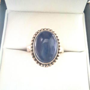 May include: A silver ring with a dark blue oval gemstone set in a beaded bezel.