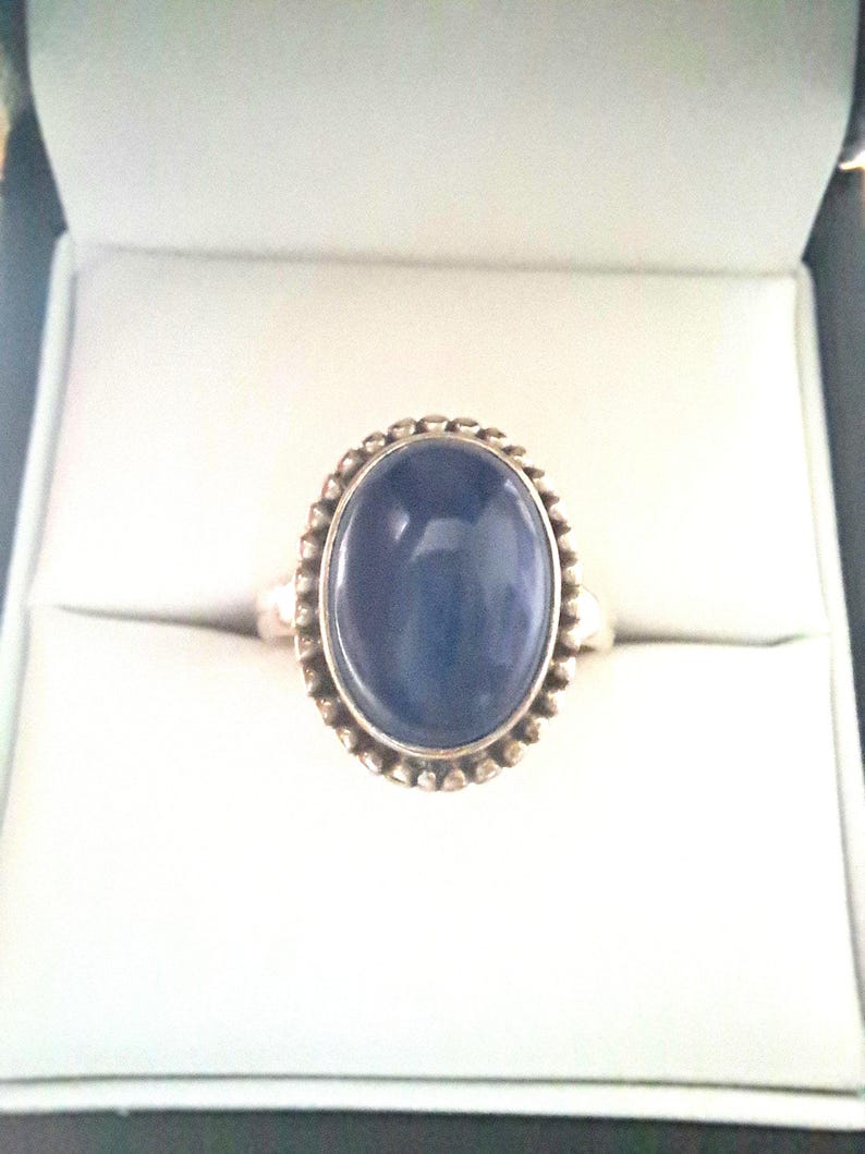 May include: A silver ring with a dark blue oval gemstone set in a beaded bezel.
