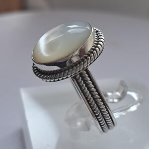 May include: A silver ring with a white oval gemstone set in a braided band.