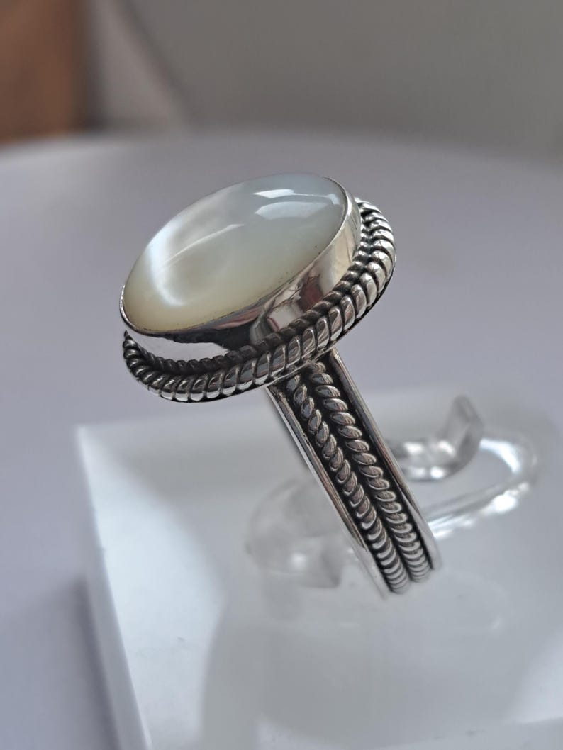 May include: A silver ring with a white oval gemstone set in a braided band.