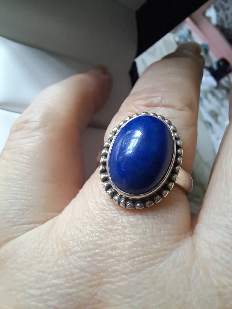 May include: A silver ring with a deep blue oval lapis lazuli gemstone set in a beaded bezel.