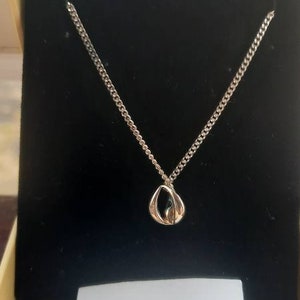 May include: A silver necklace with a delicate, open circle pendant. The necklace is displayed in a black box with a white card that reads "Dew Jewelry".