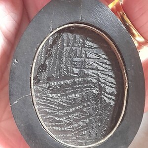 May include: A black oval pendant with a silver rim and a textured black surface inside.