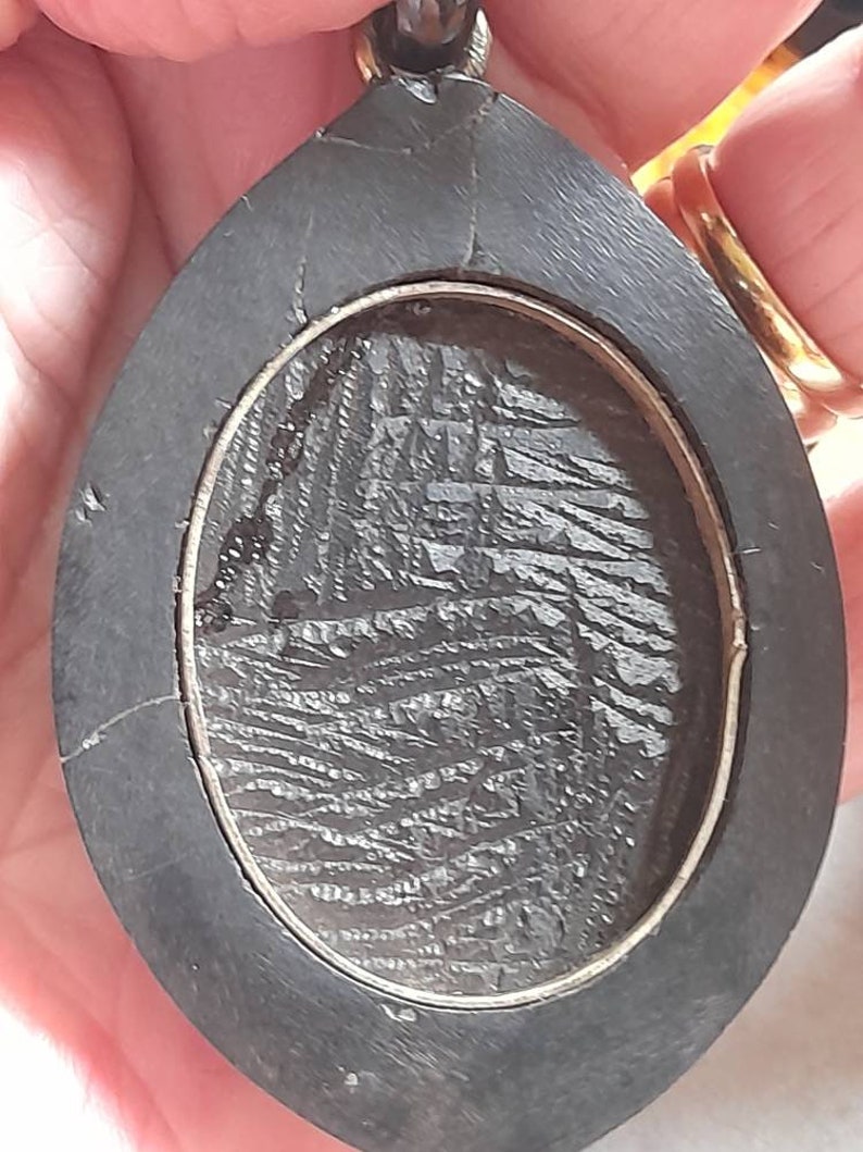 May include: A black oval pendant with a silver rim and a textured black surface inside.