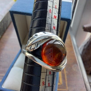 May include: A silver ring with a large amber stone set in a leaf design. The ring is on a sizing tool, showing a size 9.