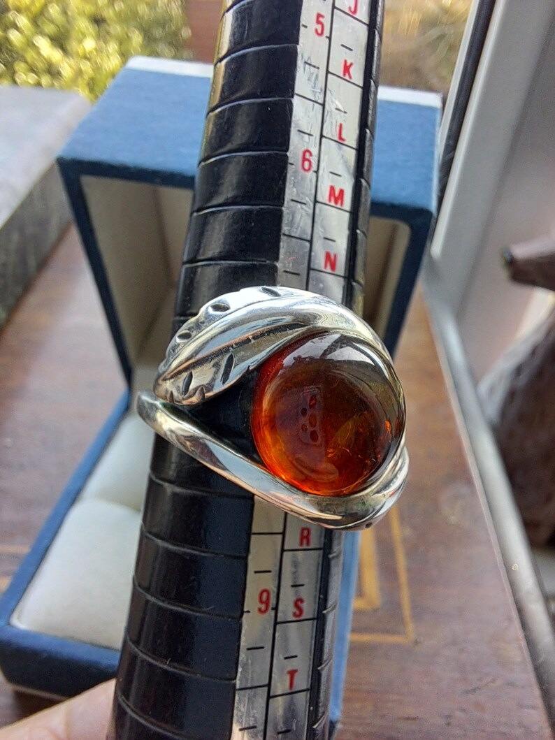 May include: A silver ring with a large amber stone set in a leaf design. The ring is on a sizing tool, showing a size 9.