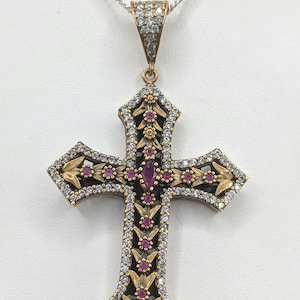 Può includere: Un ciondolo a croce con una montatura in metallo dorato con intricati motivi floreali incisi, impreziosito da piccole pietre bianche trasparenti lungo i bordi e da una serie di piccole pietre rosa rotonde e una pietra rosa centrale taglio marquise.