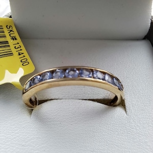 Könnte beinhalten: Ein Goldring mit einer Reihe blauer Edelsteine. Der Ring befindet sich in einer weißen Schachtel mit einem gelben Etikett, auf dem "SKU# 1314100" steht.