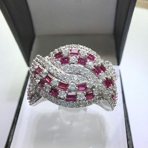 May include: A silver ring with a wave-like design featuring a row of pink square-shaped stones surrounded by smaller white round stones.