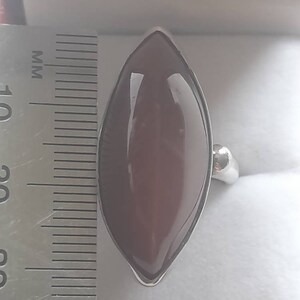 May include: A silver ring with a large, dark red, marquise-shaped gemstone. The ring is next to a ruler, showing the stone is approximately 2.5 inches long.