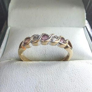 May include: A gold band ring with alternating pink and white gemstones. The ring is set in a delicate, twisted design.