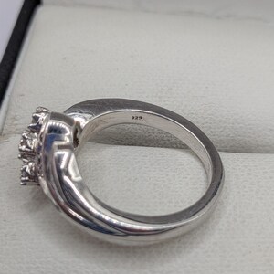 May include: A silver ring with a cluster of small, clear stones. The ring has a polished finish and a band marked with "925". The ring is set in a light-colored jewelry box.