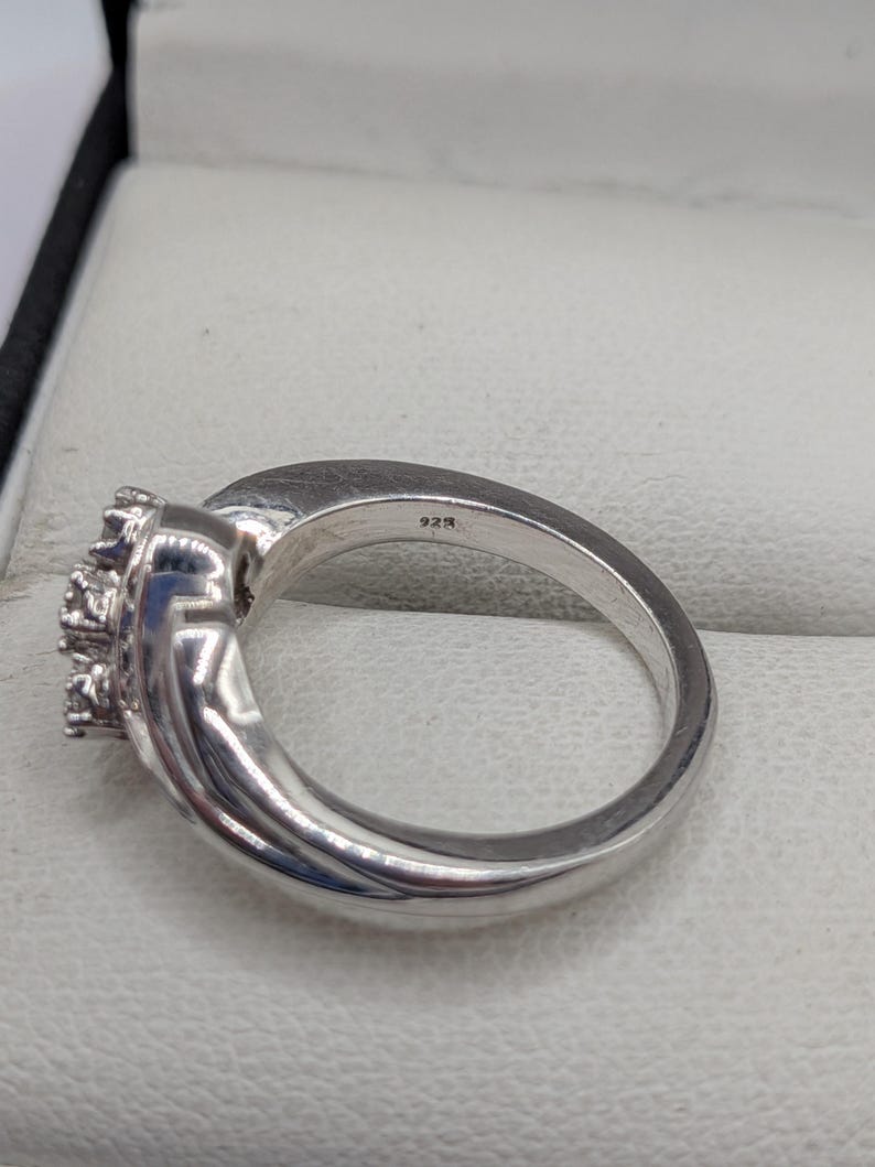 May include: A silver ring with a cluster of small, clear stones. The ring has a polished finish and a band marked with "925". The ring is set in a light-colored jewelry box.